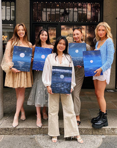 Group of women holding seascape paintings at Brush and Bubbles paint and prosecco event 
