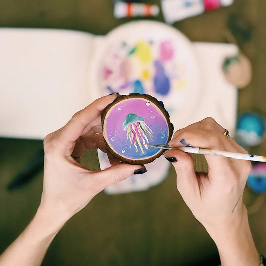 artist painting a jellyfish on a wooden disk