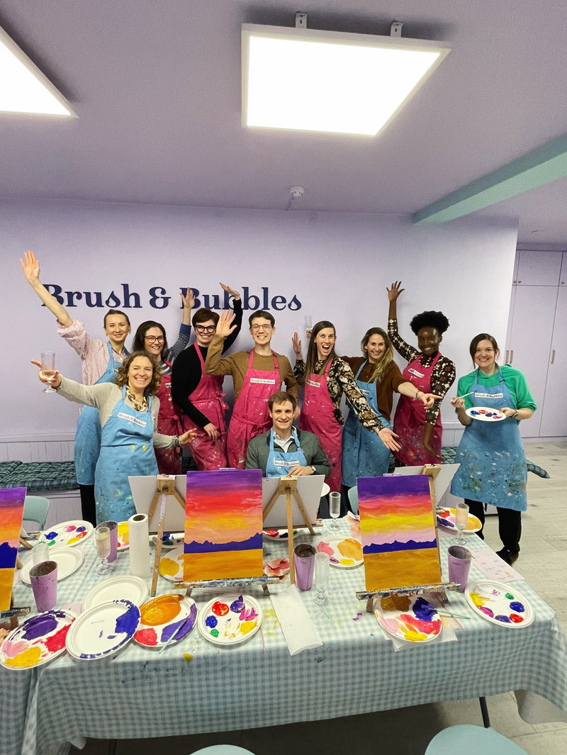 Group of people at a painting class with 'Brush & Bubbles' branding in the background.