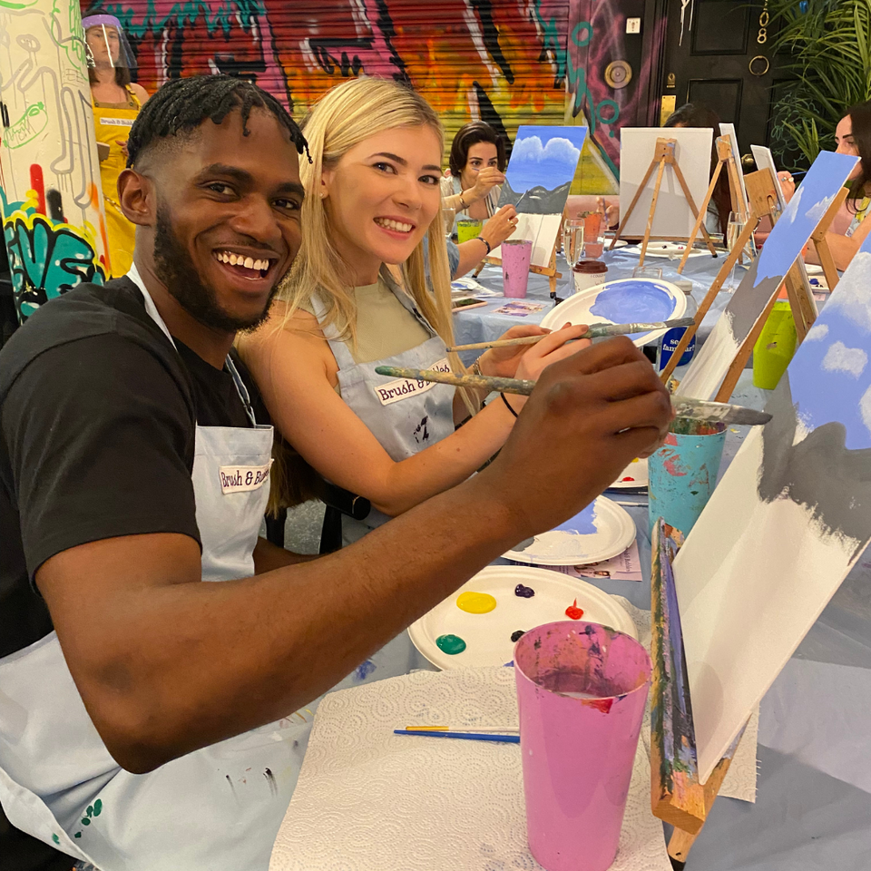 man and woman smiling whilst painting a canvas