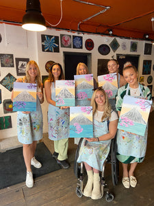group of women holding paintings of Mt. Fuji at Brush and Bubbles paint and sip event