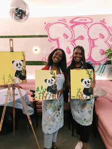 two friends holding paintings of Pandas at Brush and Bubbles art event
